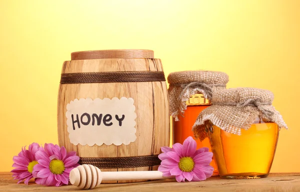 Солодкий мед в бочці і банки з мрякою на дерев'яному столі на жовтому фоні — стокове фото