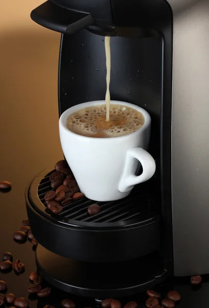 Máquina de café expresso derramando café na xícara no fundo marrom — Fotografia de Stock