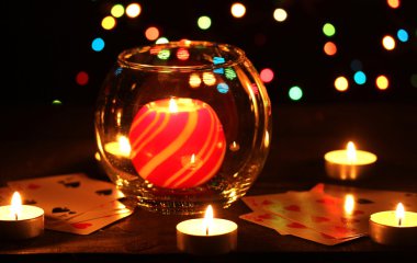 Candles and playing cards on wooden table on bright background clipart