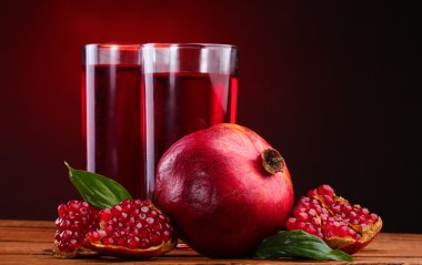 Ripe pomergranate and glasses of juice on wooden table on red background clipart