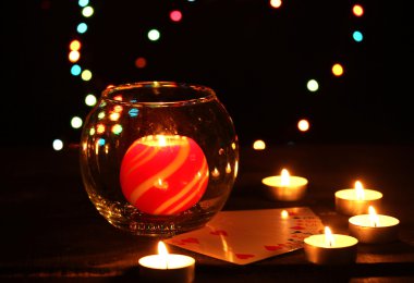 Candles and playing cards on wooden table on bright background clipart