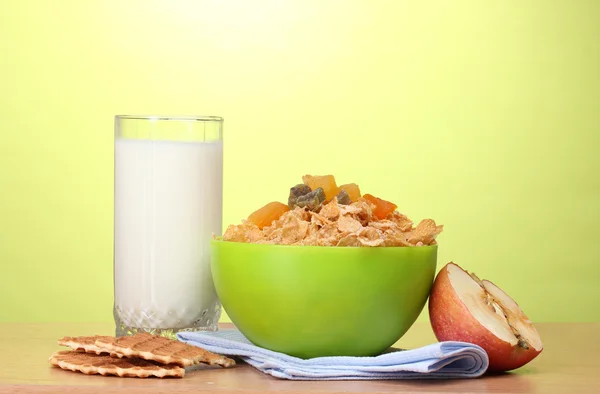 Leckere Cornflakes in grüner Schüssel, Apfel und Milchglas auf Holztisch auf grünem Hintergrund — Stockfoto