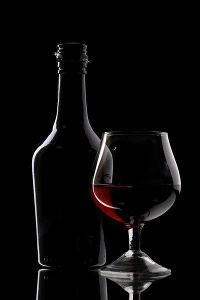 Glass of brandy and bottle on black background — Stock Photo, Image