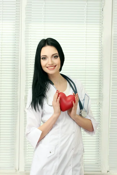 年轻漂亮的女医生用听诊器握着的心 — 图库照片