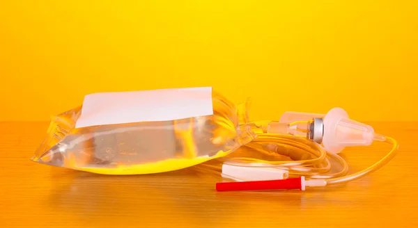 Sekantong antibiotik intravena dan infus plastik diletakkan di meja kayu dengan latar belakang kuning — Stok Foto