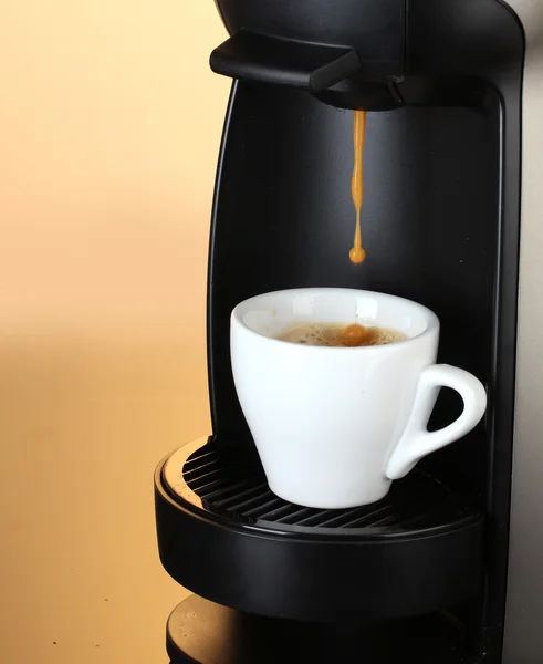 Ekspres do kawy nalewający kawę do filiżanki na brązowym tle — Zdjęcie stockowe