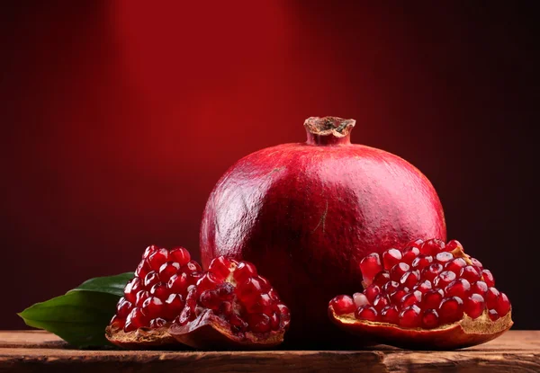Fruta de romã madura com folhas na mesa de madeira no fundo vermelho — Fotografia de Stock