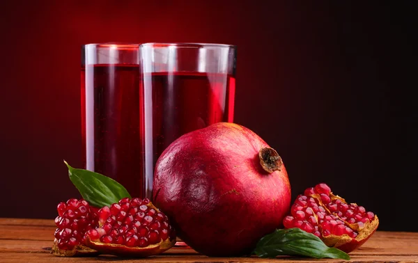 Pomergranato maduro y vasos de jugo sobre mesa de madera sobre fondo rojo — Foto de Stock