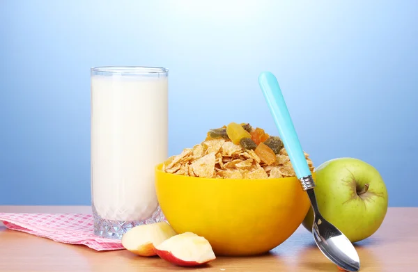 Flocos de milho saborosos em tigela amarela, maçãs e vidro de leite na mesa de madeira no fundo azul — Fotografia de Stock