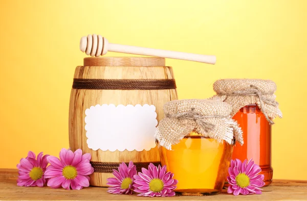 Süßer Honig in Gläsern und Fässern mit Nieselregen auf Holztisch auf gelbem Hintergrund — Stockfoto