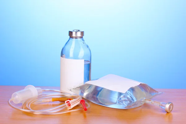 Bottiglia e sacchetto di antibiotici per via endovenosa e infusione di plastica impostato su tavolo di legno su sfondo blu — Foto Stock