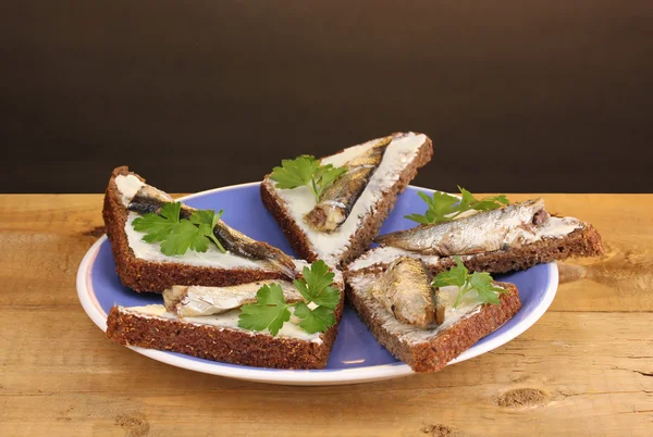 Tasty sandwiches with sprats on plate on wooden table on brown background — Stock Photo, Image