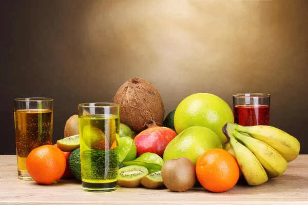 Assortment of exotic fruits and juice on wooden table on brown background — Stock Photo, Image