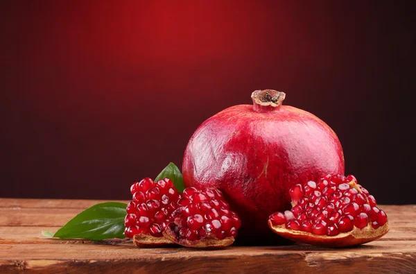 Fruta de granada madura con hojas sobre mesa de madera sobre fondo rojo — Foto de Stock