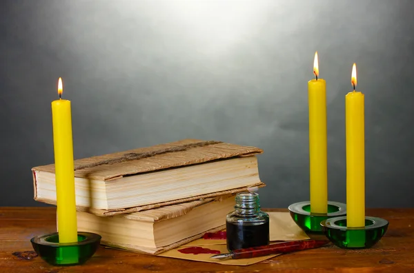 Old books, scrolls, ink pen inkwell and candles on wooden table on grey background — Stock Photo, Image