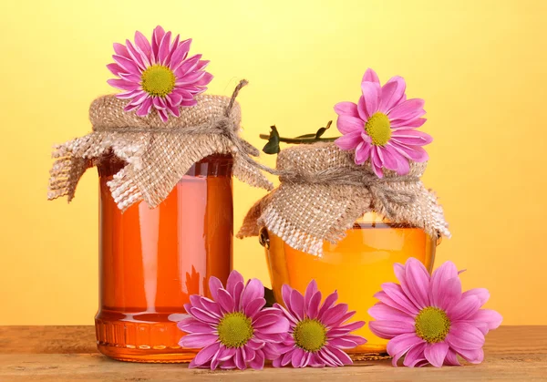 Zoete honing in potten op houten tafel op gele achtergrond — Stockfoto