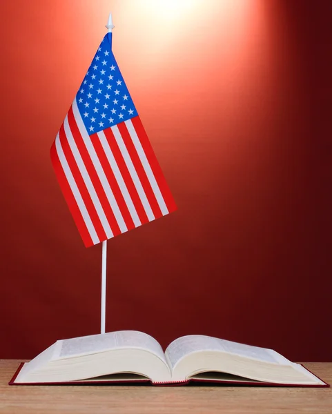 Bandeira americana no carrinho e livro sobre mesa de madeira no fundo vermelho — Fotografia de Stock