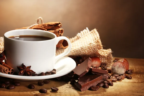 Kahve fincanı ve fasulye, tarçın, fındık ve çikolata kahverengi zemin üzerine ahşap tablo — Stok fotoğraf