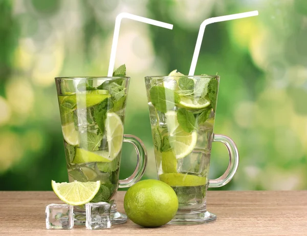 Bicchieri di cocktail con lime e menta su tavolo di legno su sfondo verde — Foto Stock