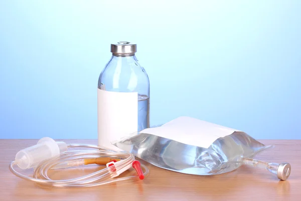 Bottiglia e sacchetto di antibiotici per via endovenosa e infusione di plastica impostato su tavolo di legno su sfondo blu — Foto Stock