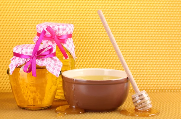 stock image Jars of honey, bowl and wooden drizzler with honey on yellow honeycomb background