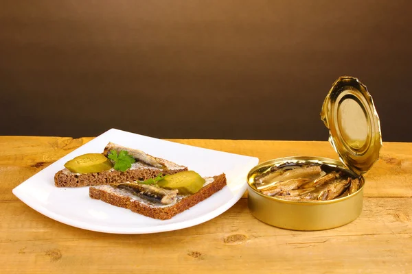 stock image Tasty sandwiches with sprats on plate on wooden table on brown background