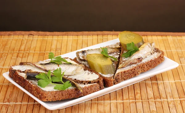 Läckra smörgåsar med skarpsill på plattan på trä matta på brun bakgrund — Stockfoto