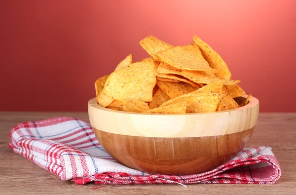 Tasty potato chips in wooden bowl on wooden table on red background — Stock Photo, Image