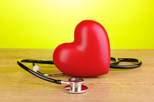 Medical stethoscope and heart on wooden table on green background — Stock Photo, Image