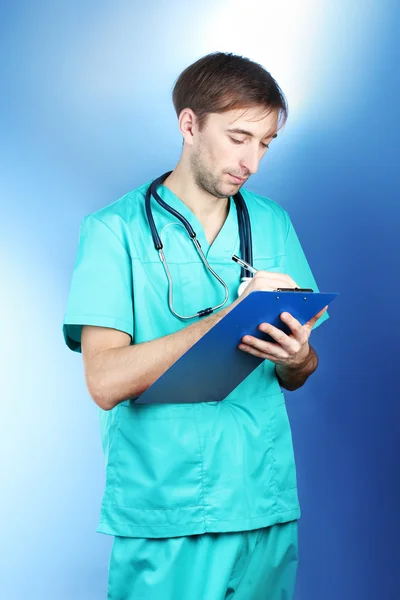 Άνθρωπος νέος γιατρός με το στηθοσκόπιο και φάκελο σε μπλε φόντο — Φωτογραφία Αρχείου