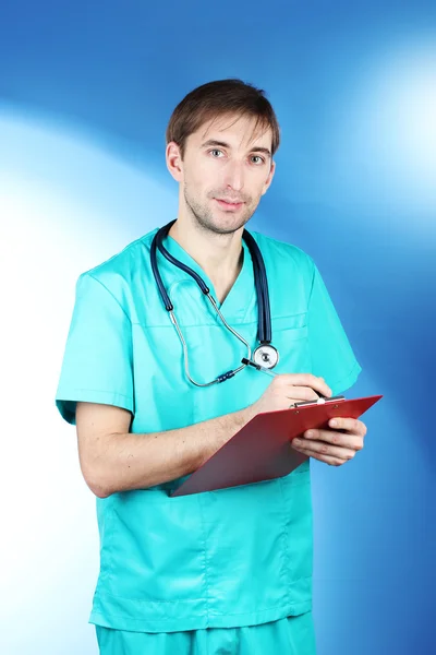 Молодой врач со стетоскопом и папкой на синем фоне — стоковое фото