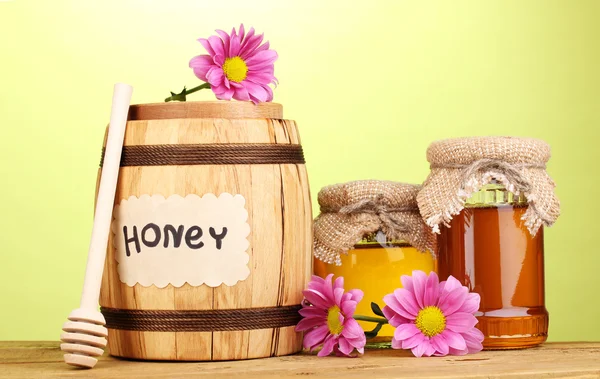 Солодкий мед в бочці і банки з мрякою на дерев'яному столі на зеленому фоні — стокове фото