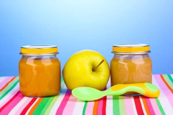 Jars of baby puree with spoon on napkin on blue background — Stock Photo, Image