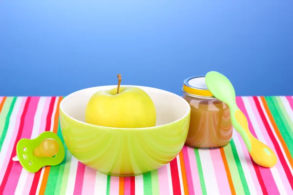 Jar of baby puree with plate and spoon on napkin on blue background — Stock Photo, Image