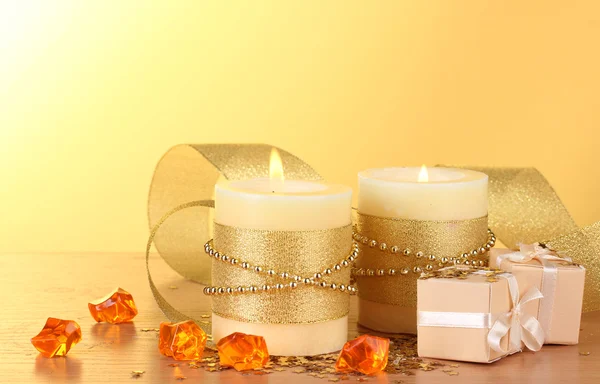 Hermosas velas y regalos en mesa de madera sobre fondo amarillo — Foto de Stock