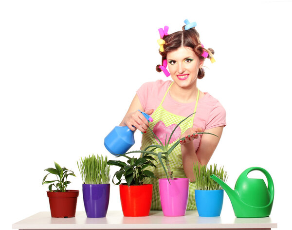 Beautiful happy young housewife sprays plants in flowerpots isolated on white