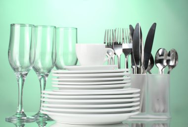 Clean plates, glasses, cup and cutlery on green background