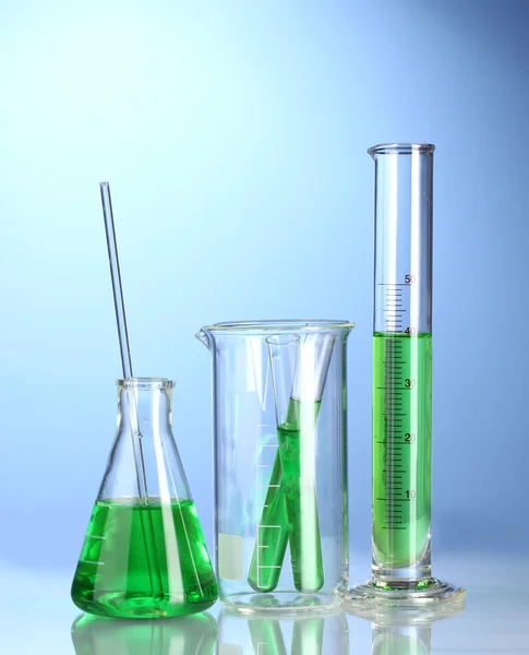 Naczynia laboratoryjne z zielona ciecz z odbiciem na niebieskim tle — Zdjęcie stockowe