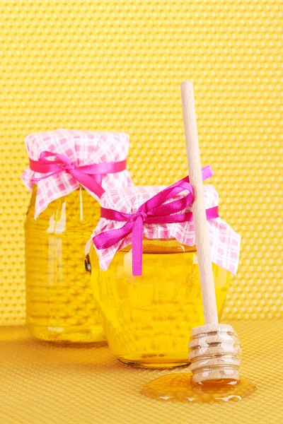 Jars of honey and wooden drizzler on yellow honeycomb background — Stock Photo, Image