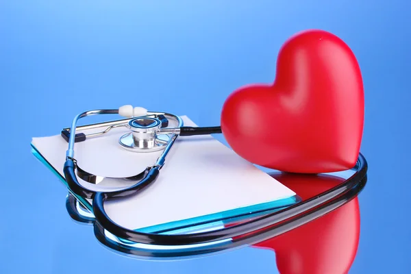 Medical stethoscope with clipboard and heart on blue background — Stock Photo, Image