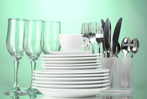 Clean plates, glasses, cup and cutlery on green background — Stok fotoğraf