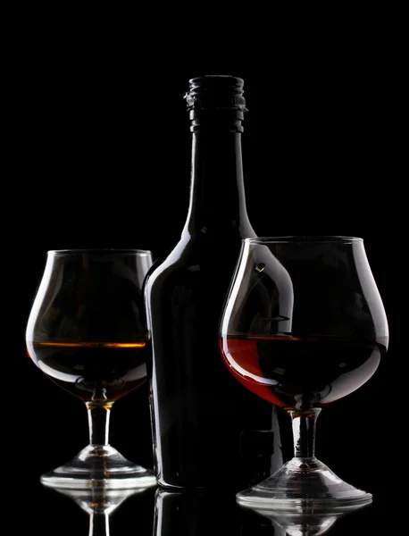 Óculos de conhaque e garrafa sobre fundo preto — Fotografia de Stock