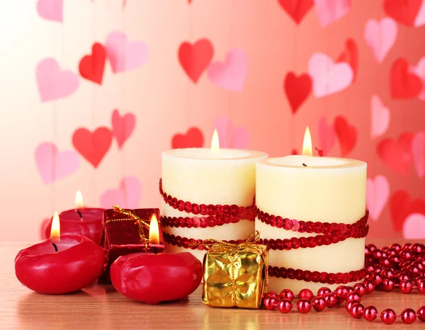 Hermosas velas con una decoración romántica sobre una mesa de madera sobre un fondo rojo —  Fotos de Stock