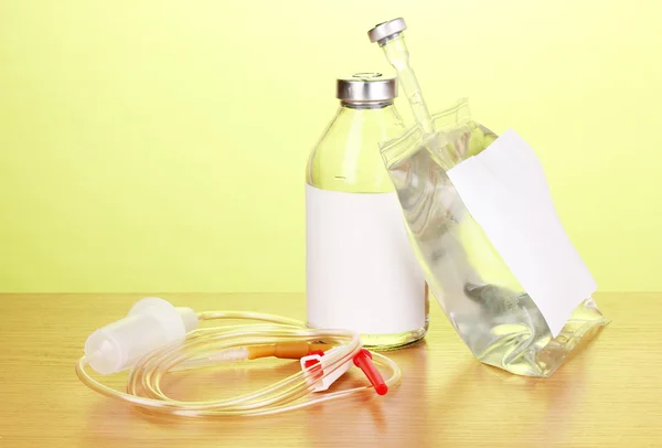 Bottle and bag of intravenous antibiotics and plastic infusion set on wooden table on green background — Stock Photo, Image