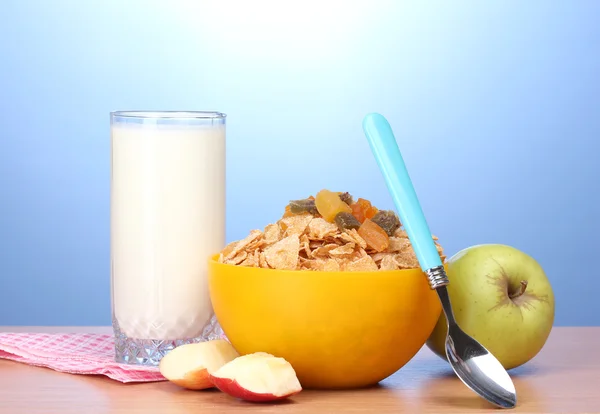 Gustosi cornflakes in ciotola gialla, mele e bicchiere di latte su tavolo di legno su sfondo blu — Foto Stock
