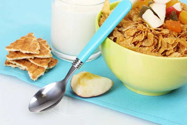Tasty cornflakes in bowl with dried fruits and glass of milk on blue napkin — Stock Photo, Image
