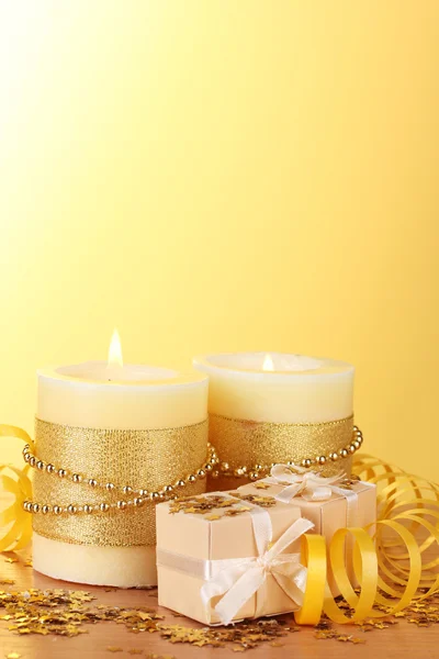 Belas velas e presentes na mesa de madeira no fundo amarelo — Fotografia de Stock