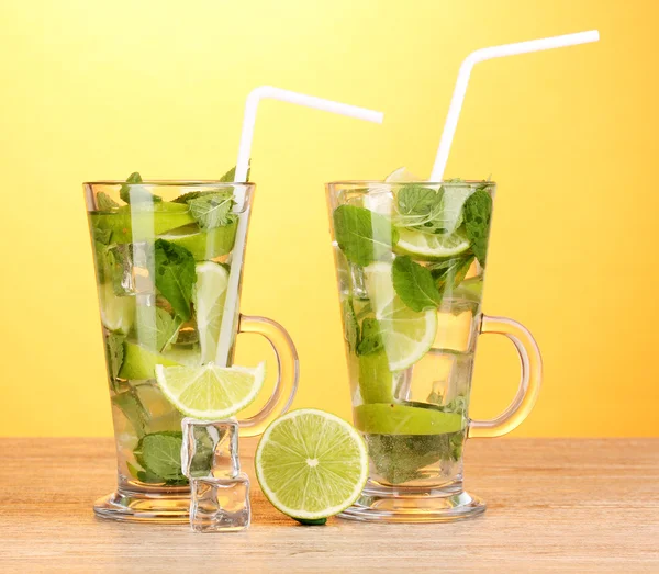 Glasses of cocktail with lime and mint on wooden table on yellow background — Stock Photo, Image