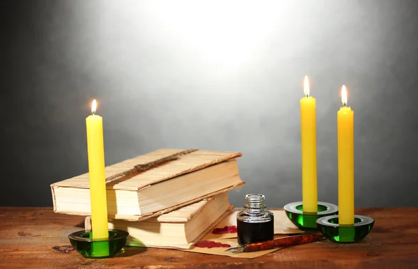 Staré knihy, svitky, inkoustové pero inkwell a svíčky na dřevěný stůl na šedém pozadí — Stock fotografie