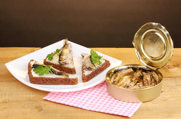 Tasty sandwiches with sprats on plate on wooden table on brown background — Stock Photo, Image